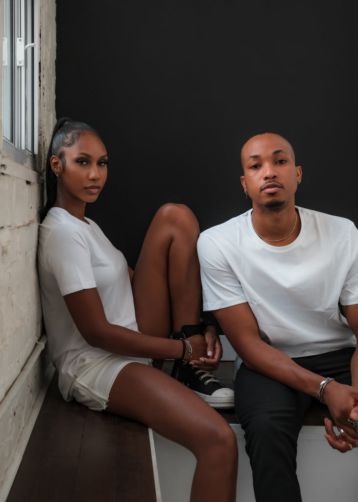 A young Black woman and man are posing in plain white t-shirts for the cover image of A Real One - the new fashion company launched by Shaun King designed to shake up the supply chain to be Black-owned from farm to closet.  